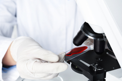Photo of Scientist holding slide with blood sample near microscope in laboratory, closeup. Virus research