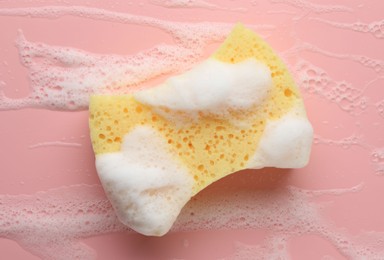 Yellow sponge with foam on pink background, top view