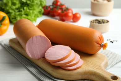 Photo of Board with tasty boiled sausages on white wooden table, closeup