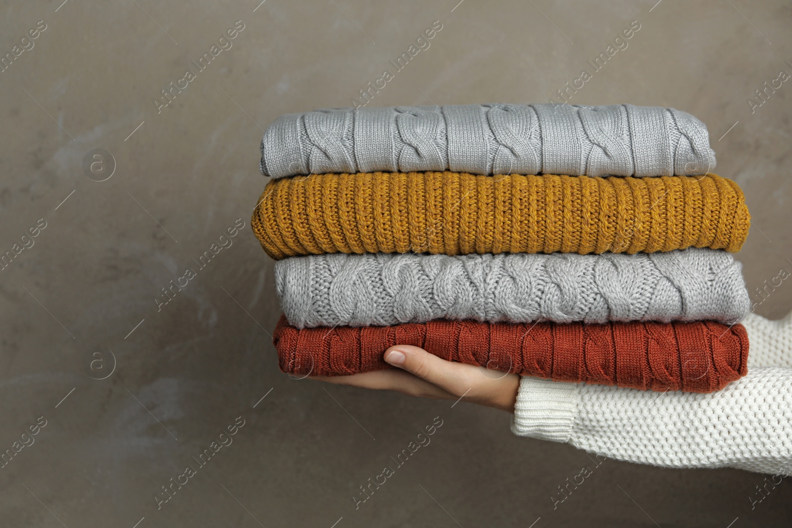 Photo of Woman holding stack of warm clothes on grey background, closeup. Autumn season