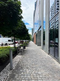 Photo of Sidewalk between modern buildings and trees along road in city