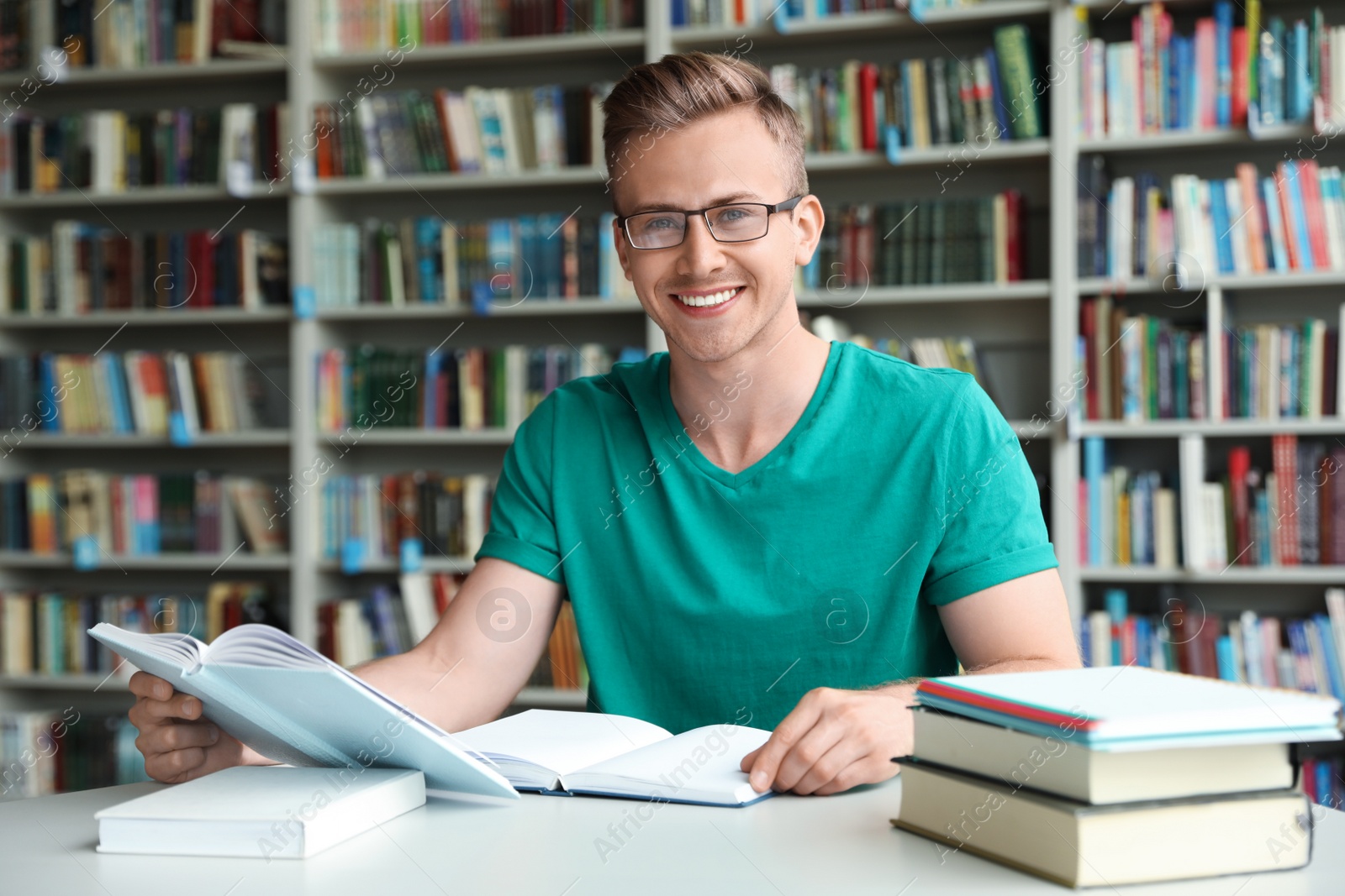 Photo of Young man with books at table in library