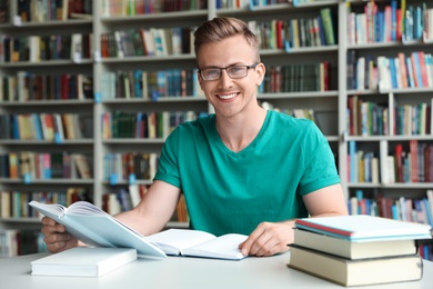 Photo of Young man with books at table in library