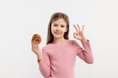 Cute girl with chocolate chip cookie showing OK gesture on white background