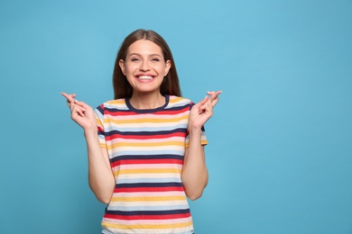 Portrait of hopeful young woman with crossed fingers on light blue background