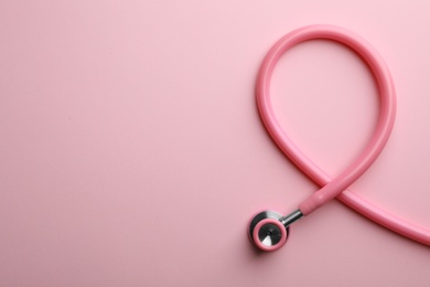 Photo of Pink stethoscope folded like awareness ribbon on color background, top view with space for text. Breast cancer concept