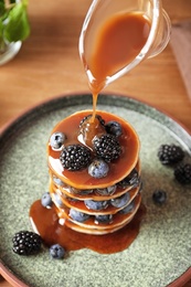 Photo of Pouring syrup onto tasty pancakes with berries on plate