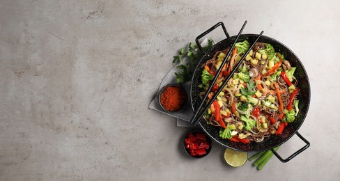 Photo of Stir-fry. Tasty noodles with meat in wok, chopsticks and ingredients on grey textured table, flat lay. Space for text