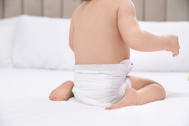 Photo of Cute little baby in diaper on bed, closeup