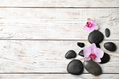 Stones with orchid flowers and space for text on white wooden background, flat lay. Zen lifestyle