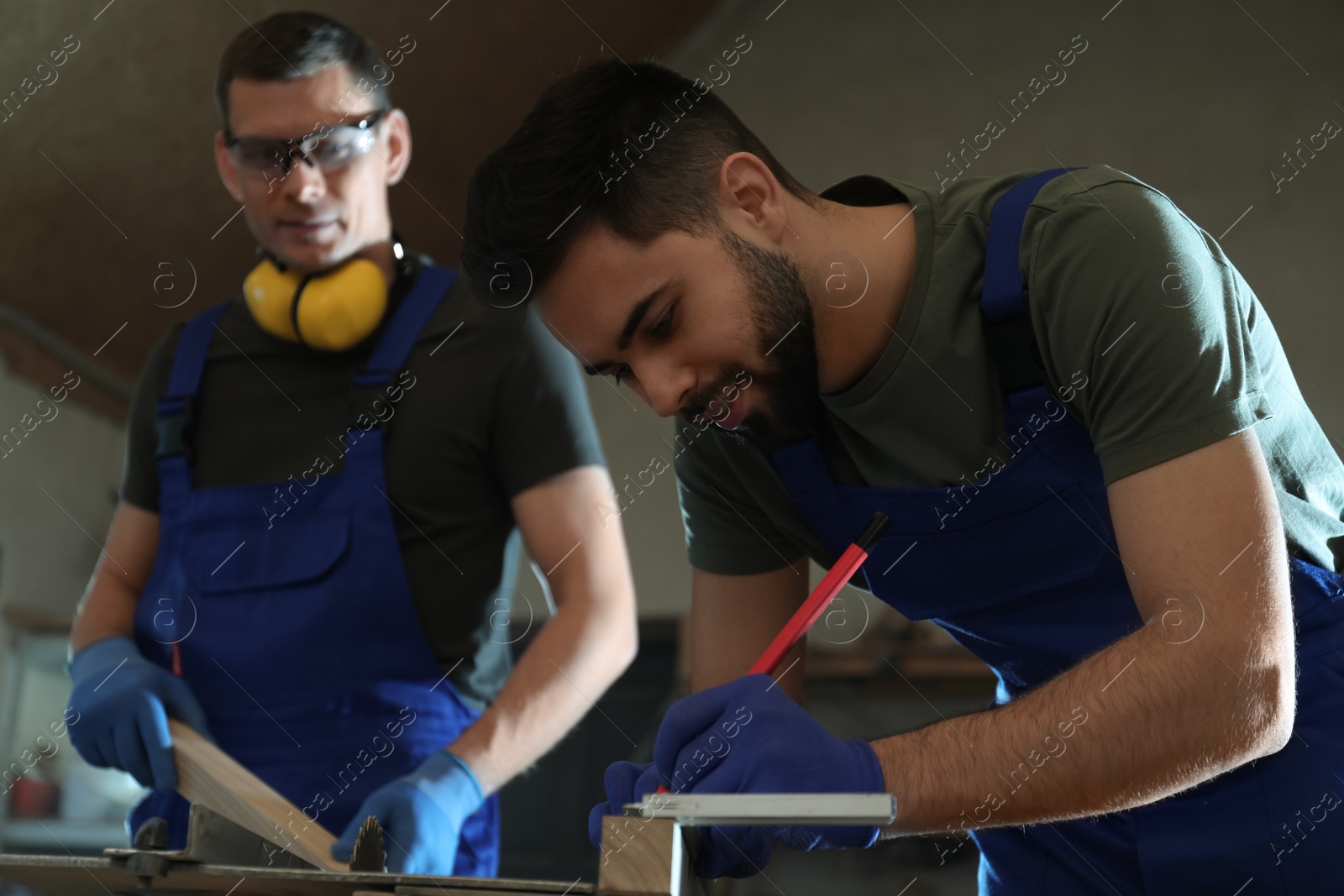 Photo of Professional carpenter making mark on wooden bar in workshop