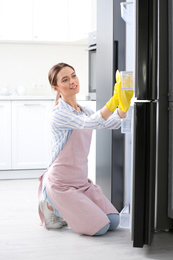 Photo of Woman in rubber gloves cleaning refrigerator at home