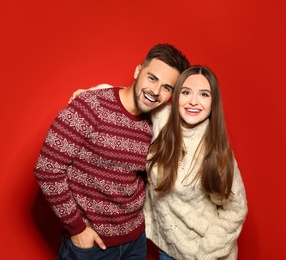 Couple wearing Christmas sweaters on red background