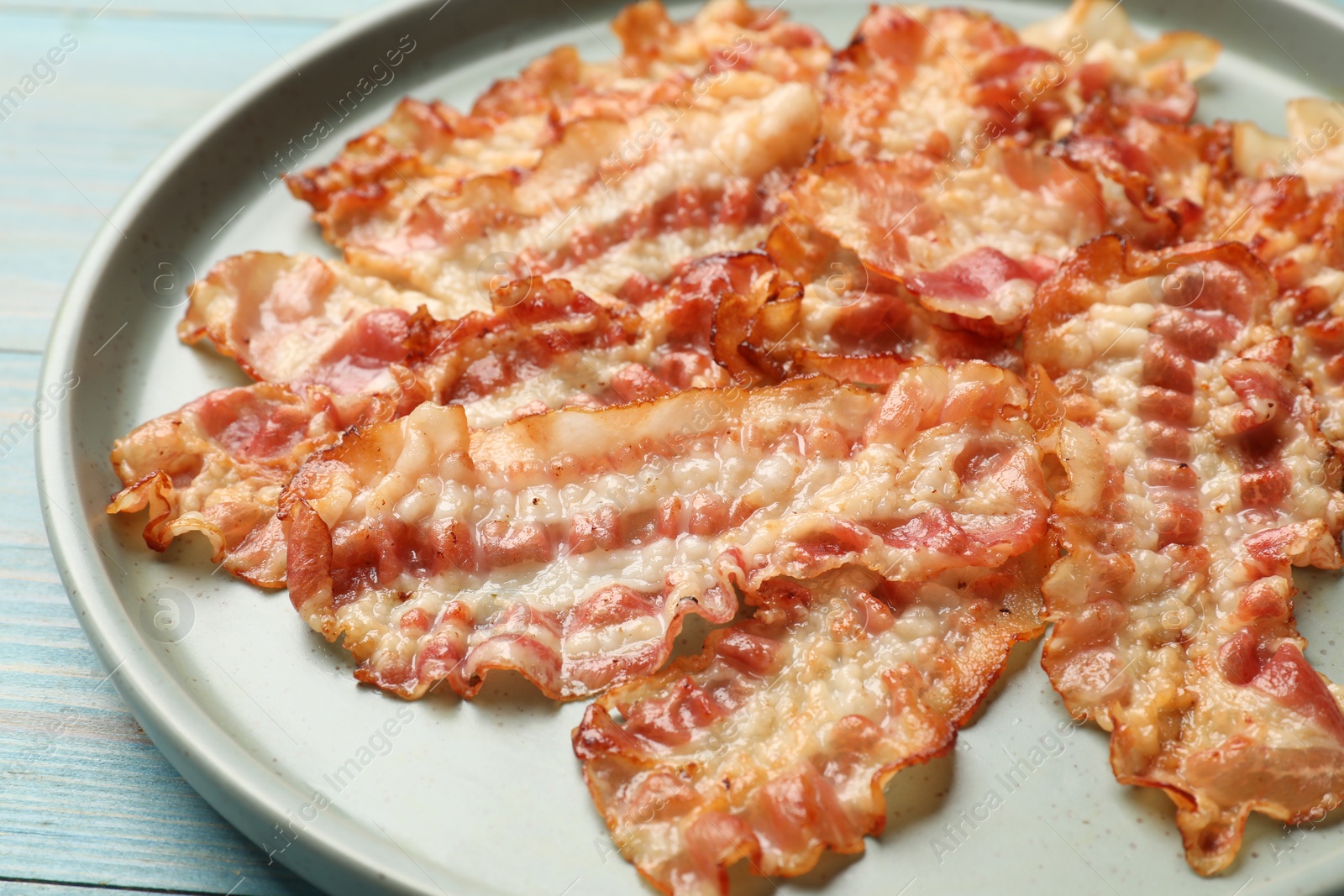 Photo of Delicious fried bacon slices on blue wooden table, closeup