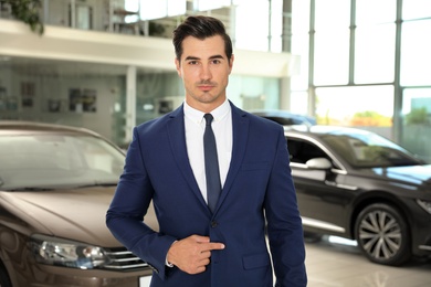 Photo of Young salesman near new car in modern dealership