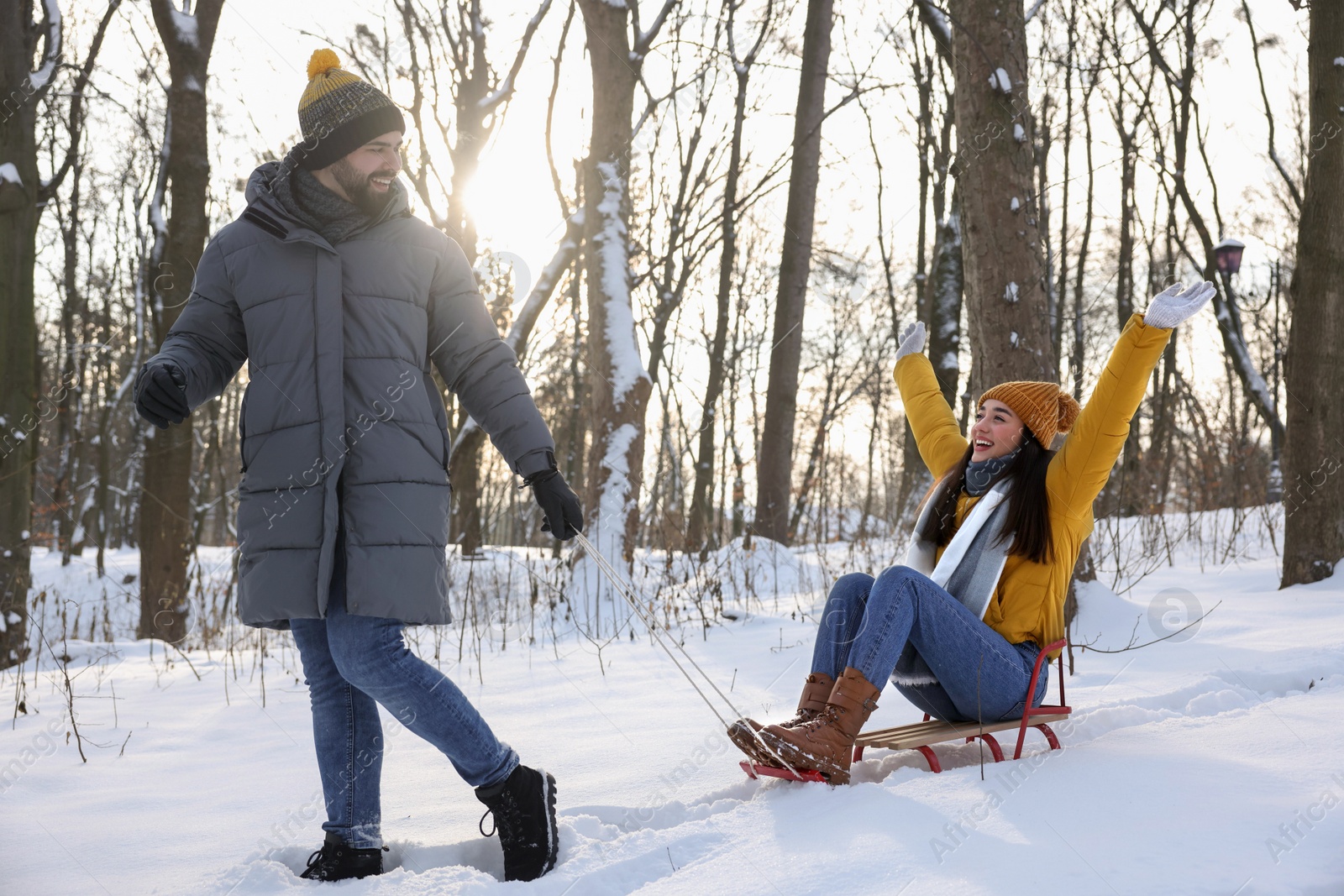 Photo of Happy young man pulling his girlfriend in sleigh outdoors on winter day