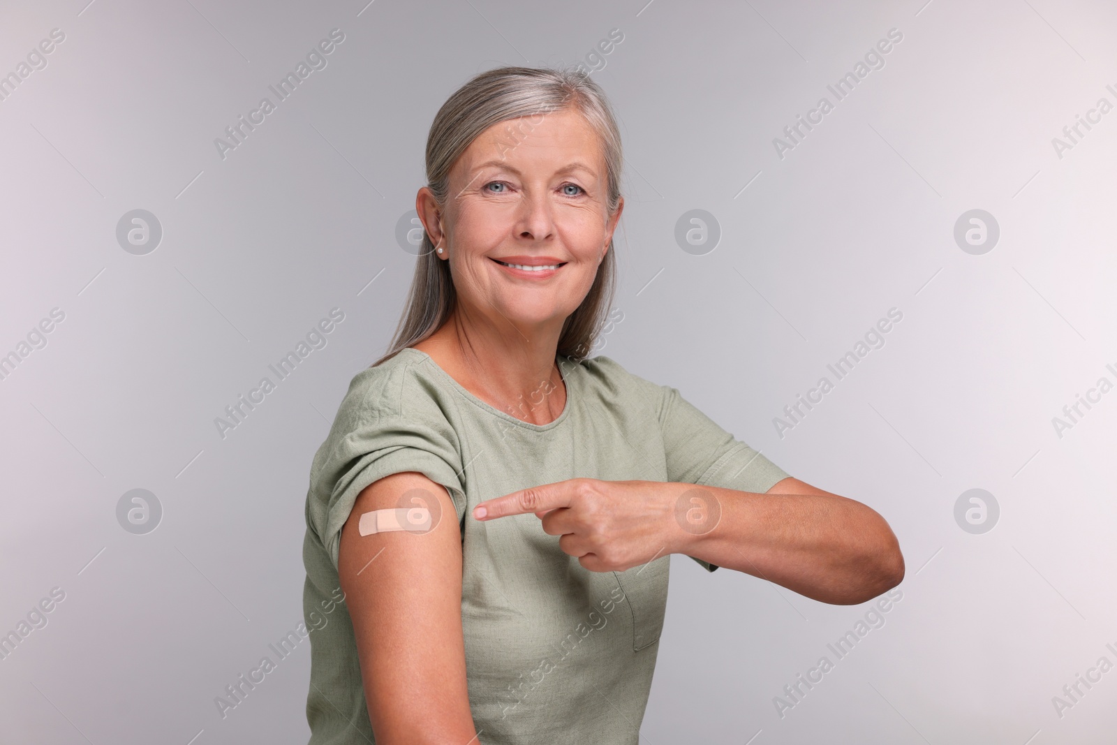 Photo of Senior woman pointing at adhesive bandage after vaccination on light grey background