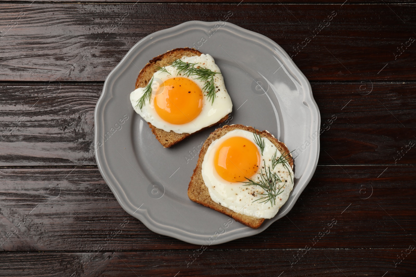 Photo of Plate with tasty fried eggs, slices of bread and dill on dark wooden table, top view