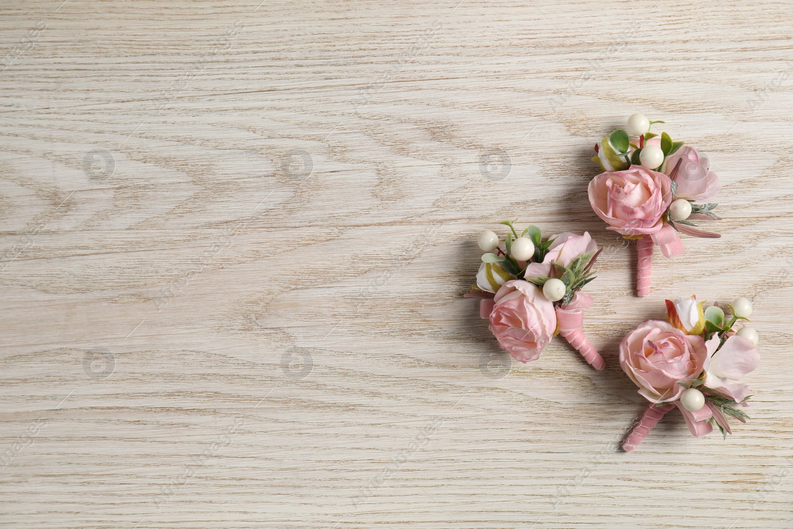 Photo of Stylish pink boutonnieres on white wooden table, flat lay. Space for text