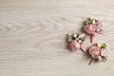 Photo of Stylish pink boutonnieres on white wooden table, flat lay. Space for text