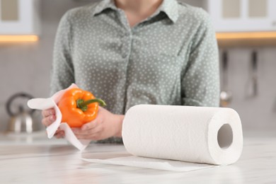Photo of Woman wiping bell pepper with paper towel at white marble table in kitchen, selective focus. Space for text