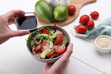 Photo of Woman adding soy sauce to tasty salad at white wooden table, closeup