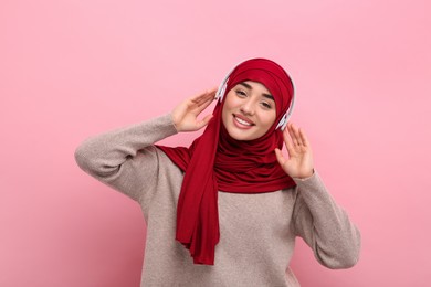 Photo of Portrait of Muslim woman in hijab and headphones on pink background