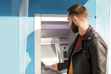 Photo of Young man taking money from cash machine outdoors