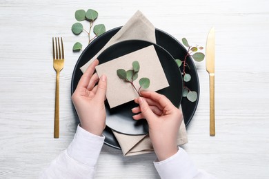 Photo of Woman decorating table setting with eucalyptus leaves, top view
