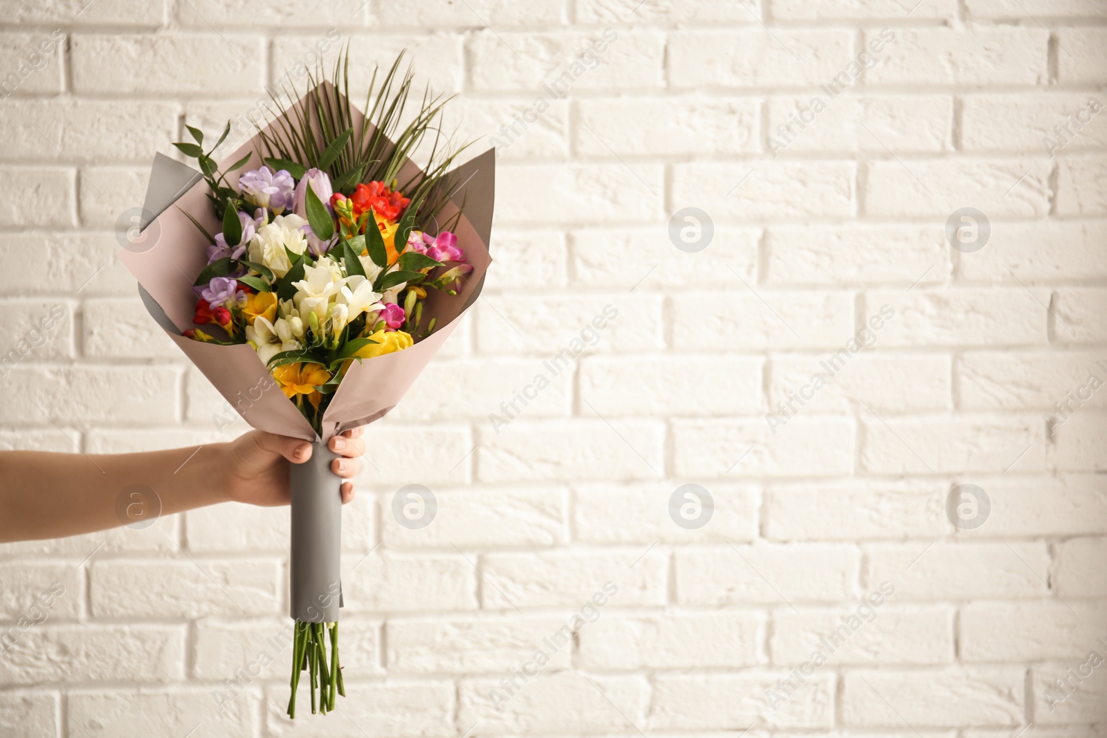 Photo of Woman with beautiful bouquet of freesia flowers on brick wall background