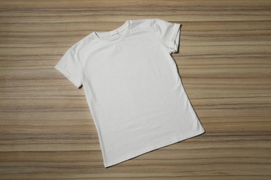 Stylish white T-shirt on wooden table, top view