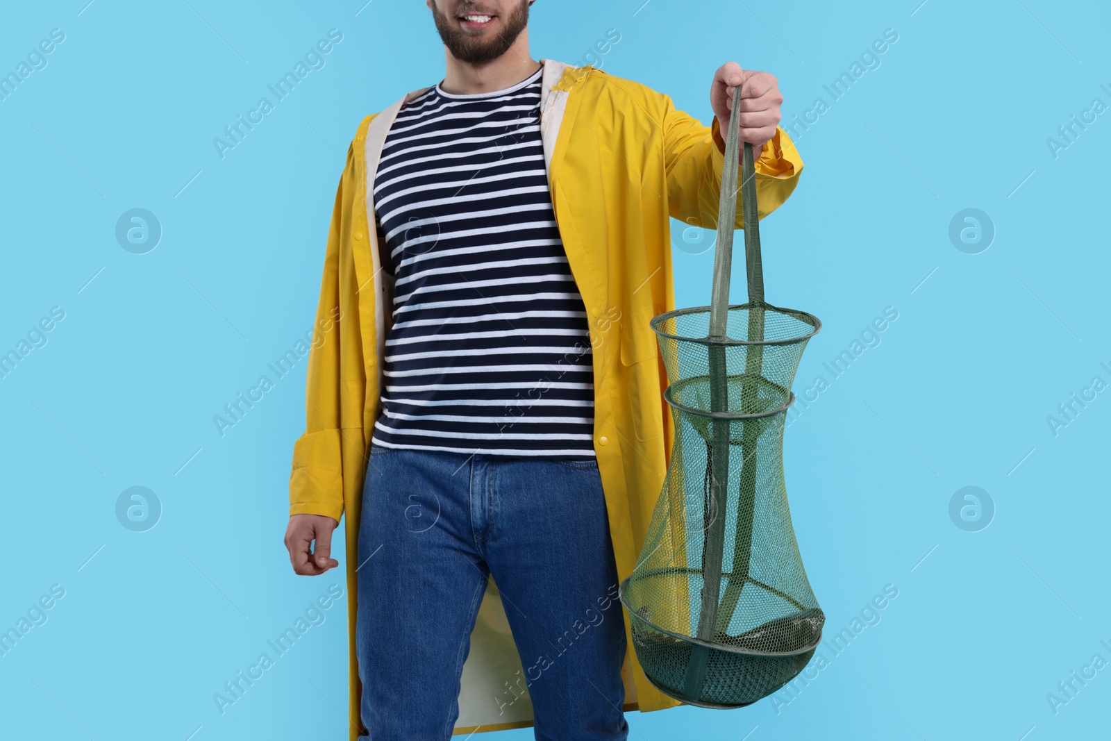 Photo of Fisherman holding fishing net with catch on light blue background, closeup