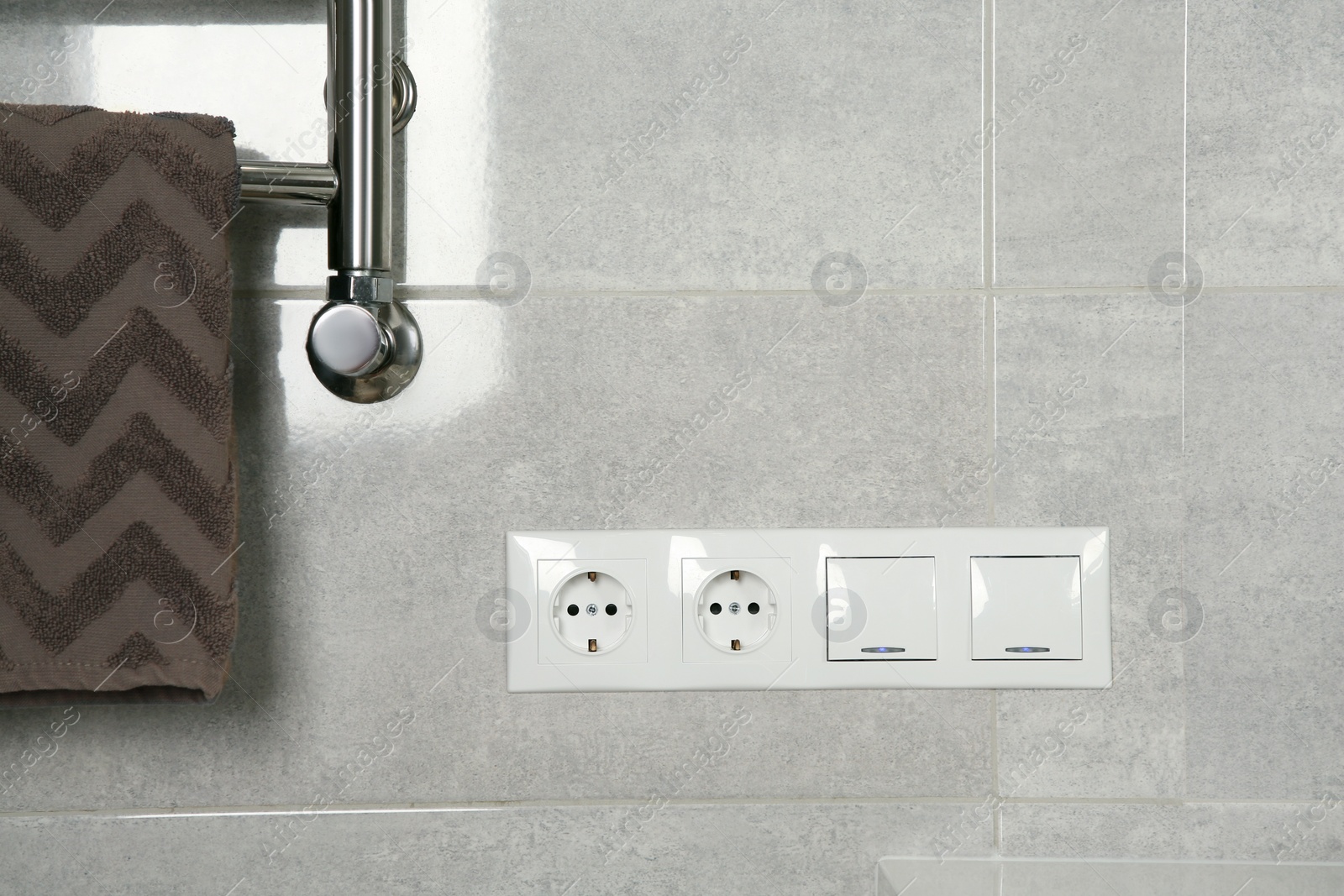 Photo of Light switches and power sockets near heated towel rail on wall in bathroom