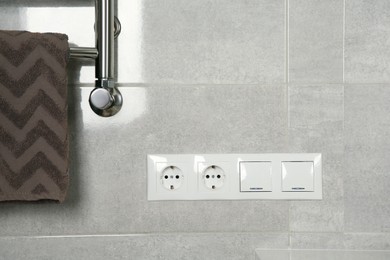 Light switches and power sockets near heated towel rail on wall in bathroom