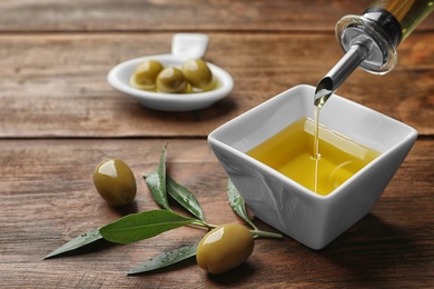 Pouring fresh olive oil into bowl on table