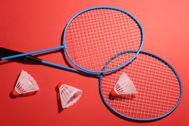 Photo of Badminton rackets and shuttlecocks on red background, flat lay