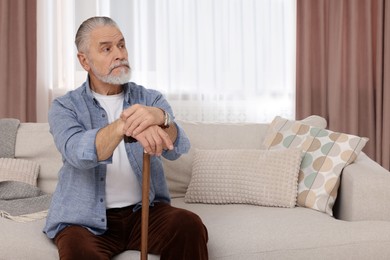 Photo of Senior man with walking cane sitting on sofa at home. Space for text