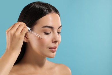 Photo of Beautiful young woman applying serum onto her face on light blue background. Space for text