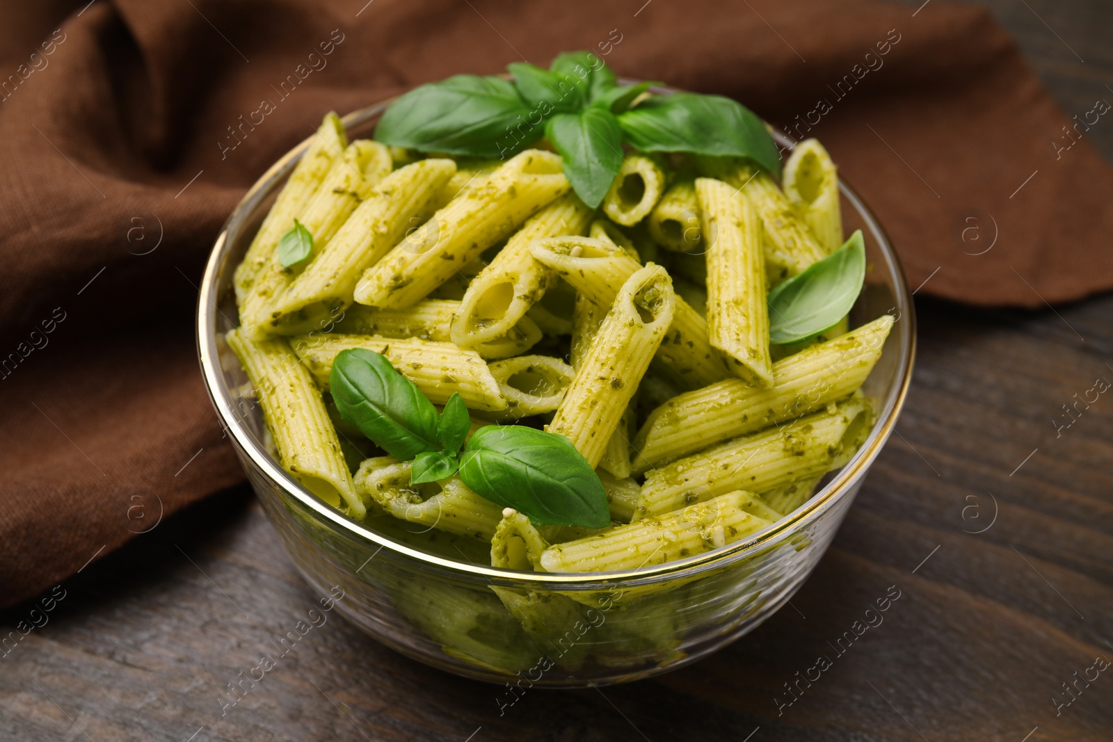 Photo of Delicious pasta with pesto sauce and basil on wooden table, closeup