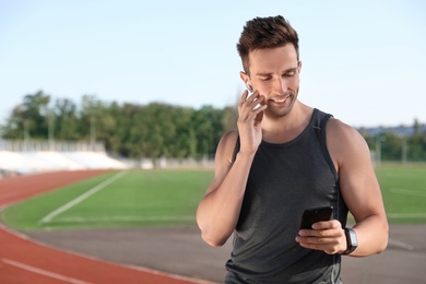 Young sportsman with wireless earphones and smartphone at stadium