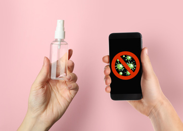 Image of Sanitizing mobile devices during coronavirus outbreak. Woman with smartphone and antiseptic spray on pink background, closeup