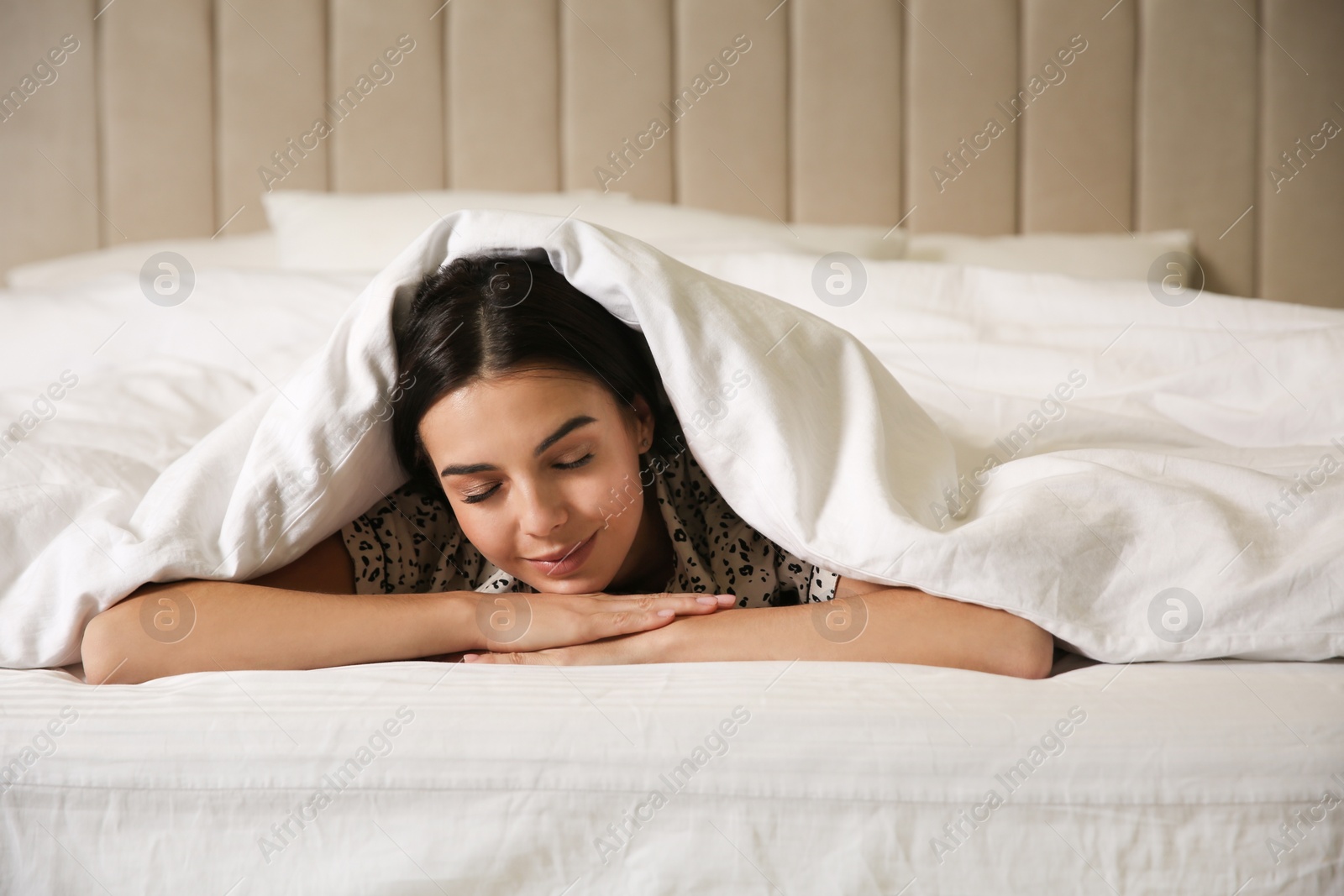 Photo of Young woman lying in bed covered with white blanket
