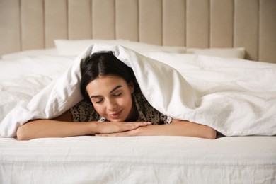 Young woman lying in bed covered with white blanket