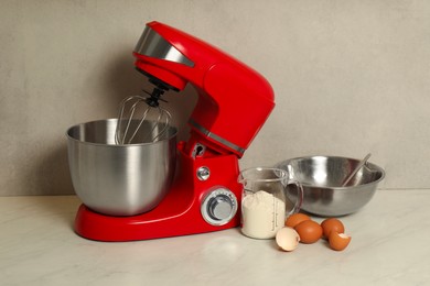 Photo of Modern red stand mixer, eggs, container with flour and bowl on white marble table