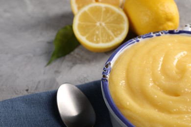 Delicious lemon curd in bowl, fresh citrus fruits and spoon on grey table, closeup