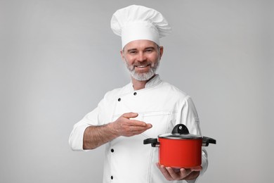 Photo of Happy chef in uniform pointing at cooking pot on grey background