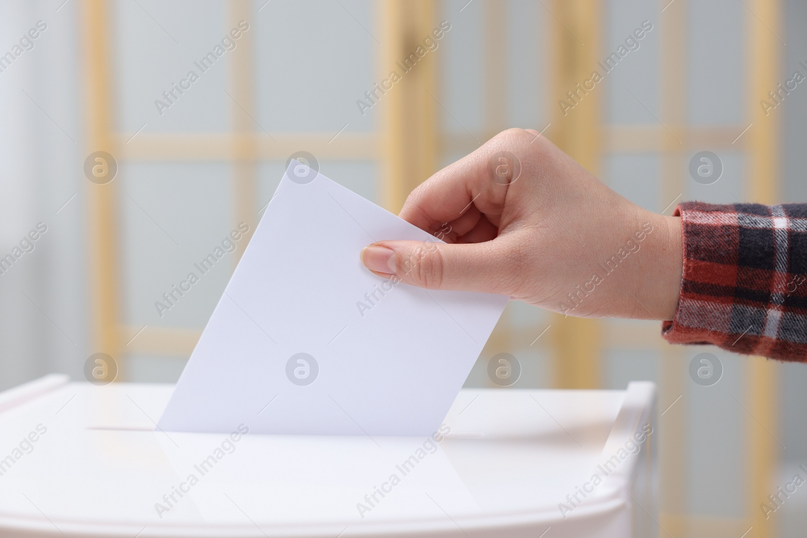 Photo of Woman putting her vote into ballot box on blurred background, closeup