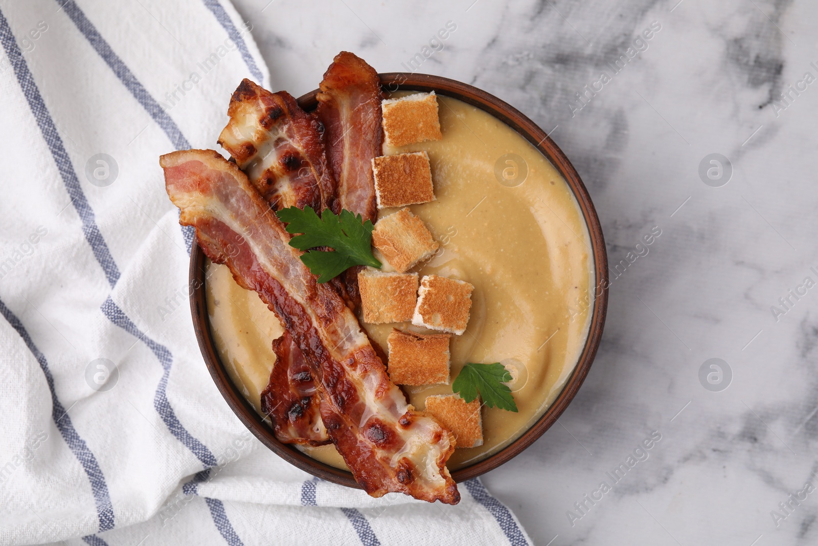 Photo of Delicious lentil soup with bacon and parsley in bowl on light marble table, top view