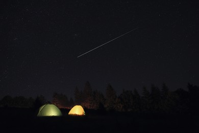 Image of Two color camping tents near forest under sky full of stars at night