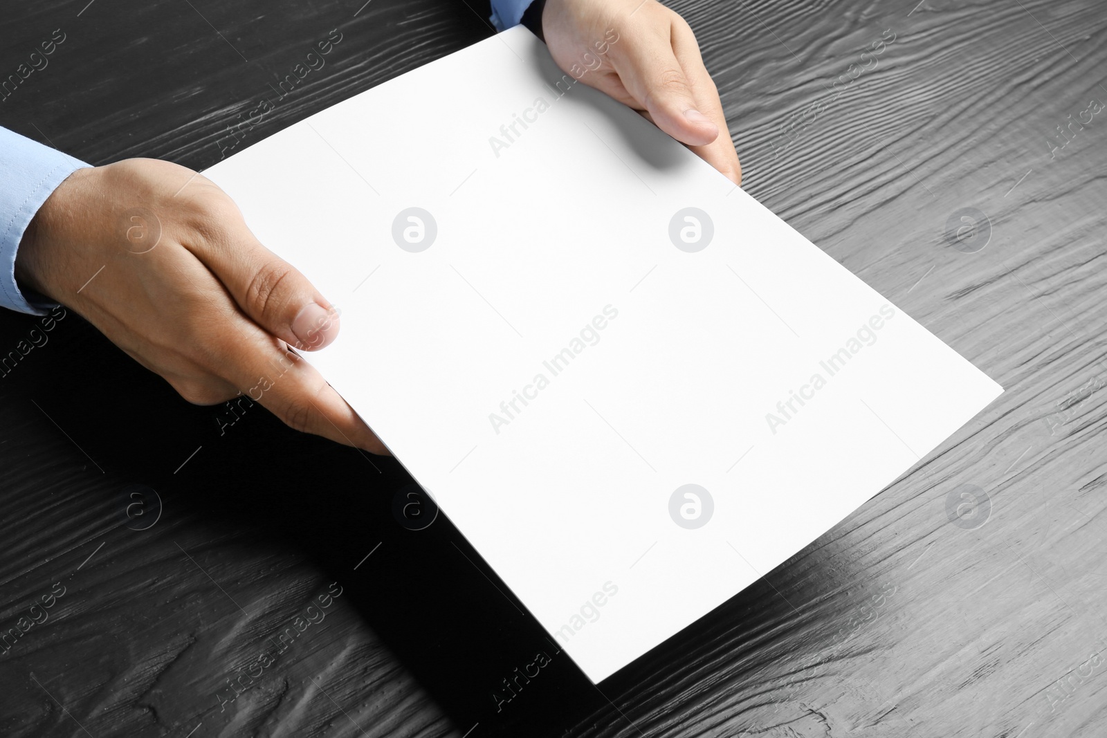 Photo of Man holding blank paper sheets for brochure at black wooden table. Mock up